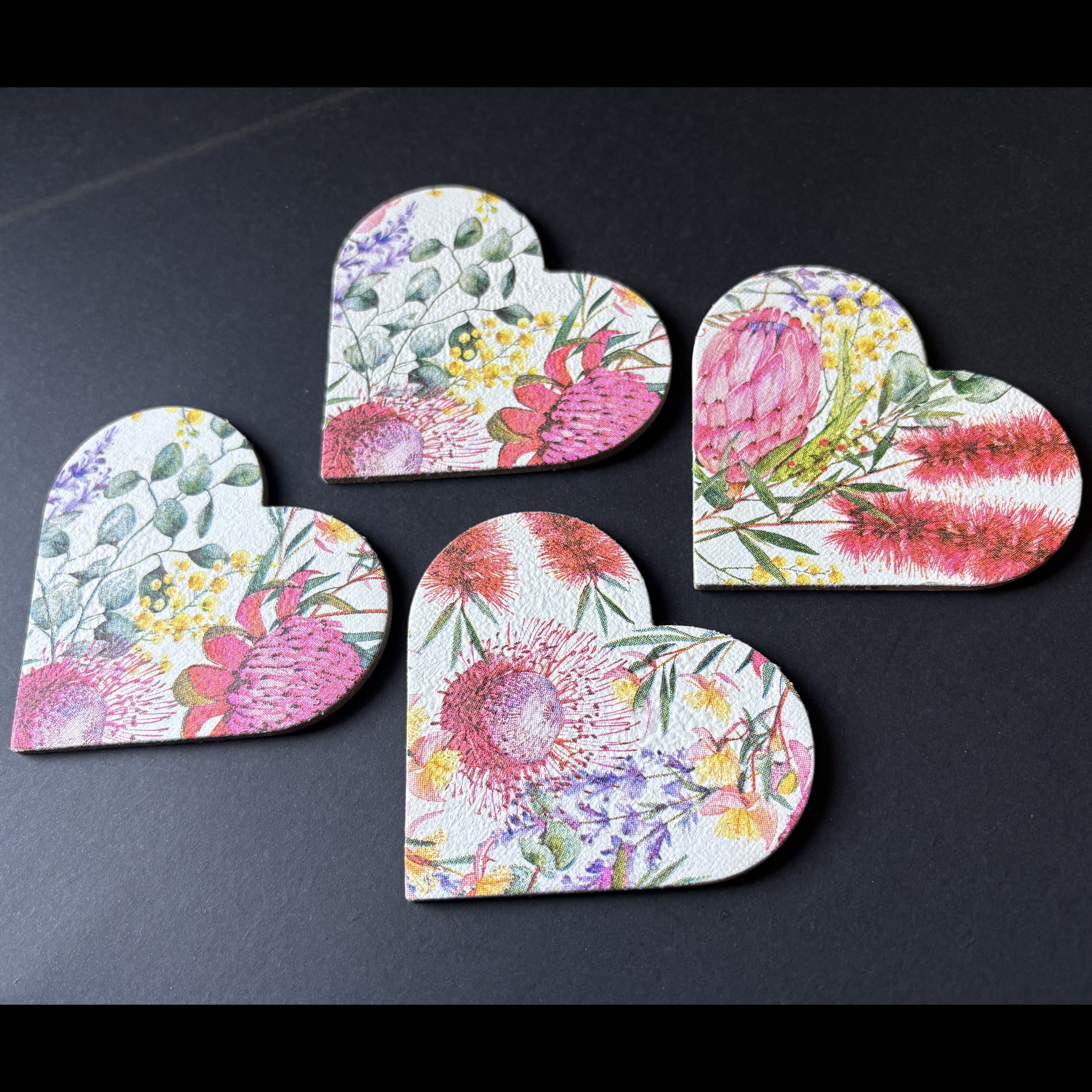 four heart-shaped magnets with a colorful watercolor floral print, arranged on a dark textured background.