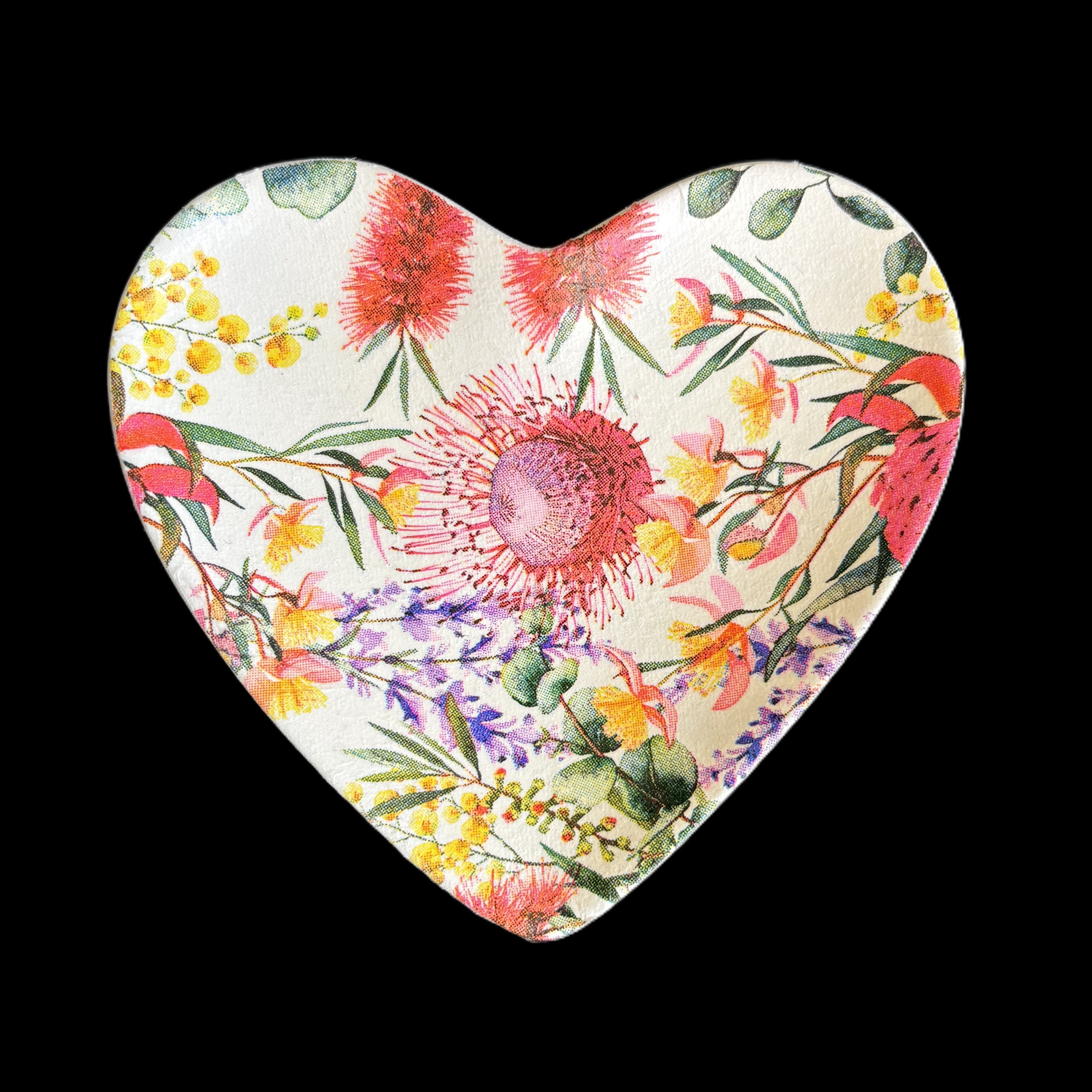 A heart-shaped ceramic trinket tray featuring a vibrant watercolor floral pattern with red, pink, yellow, and purple flowers on a cream background, set against a solid black backdrop.