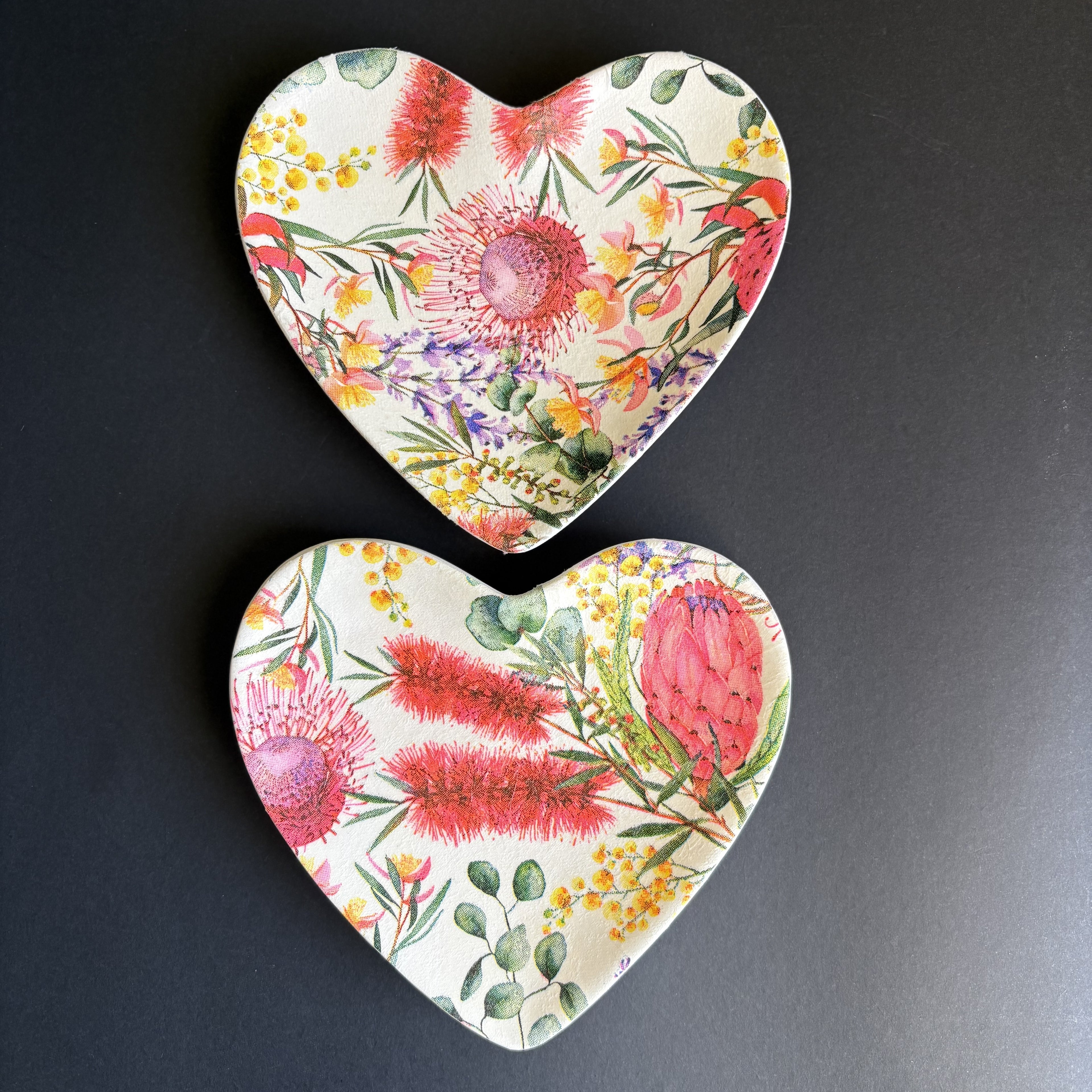 Two heart-shaped ceramic trinket tray with a vibrant watercolor floral print, displayed on a dark gray background.